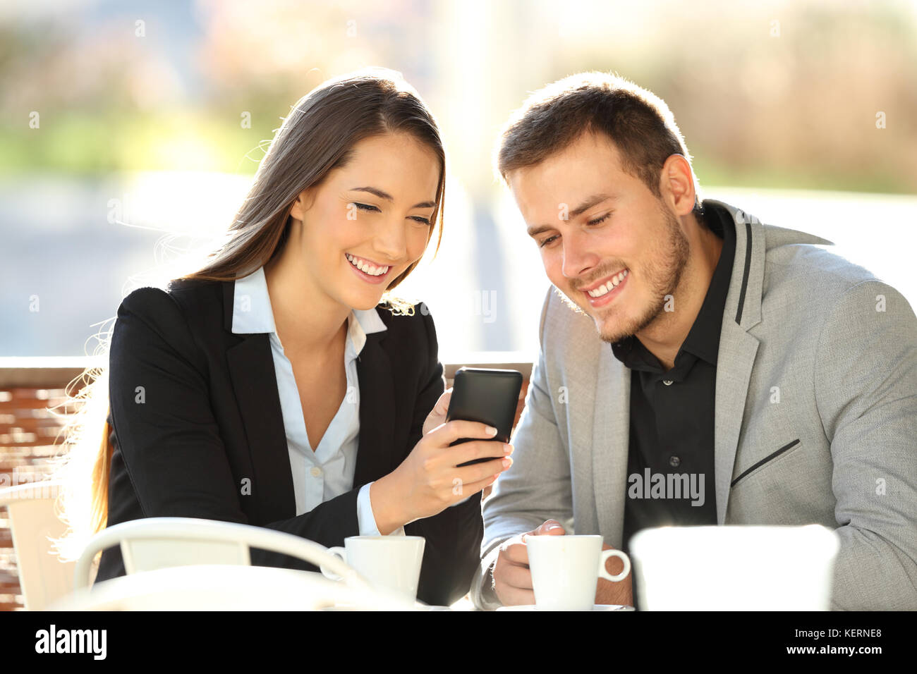 Due dirigenti felice guardare on line il contenuto in un telefono cellulare seduti in un ristorante con terrazzo Foto Stock