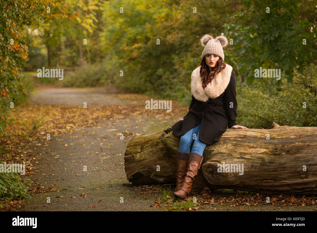 Donna vestita di cappotto e hat seduta sul log in autunno Foto Stock