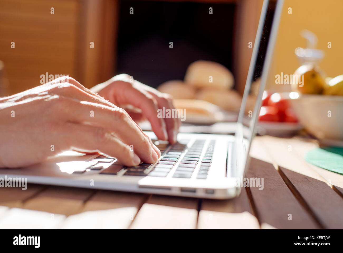 Primo piano di un giovane uomo caucasico usando un computer portatile seduti ad un tavolo di legno all'aperto durante un pasto Foto Stock
