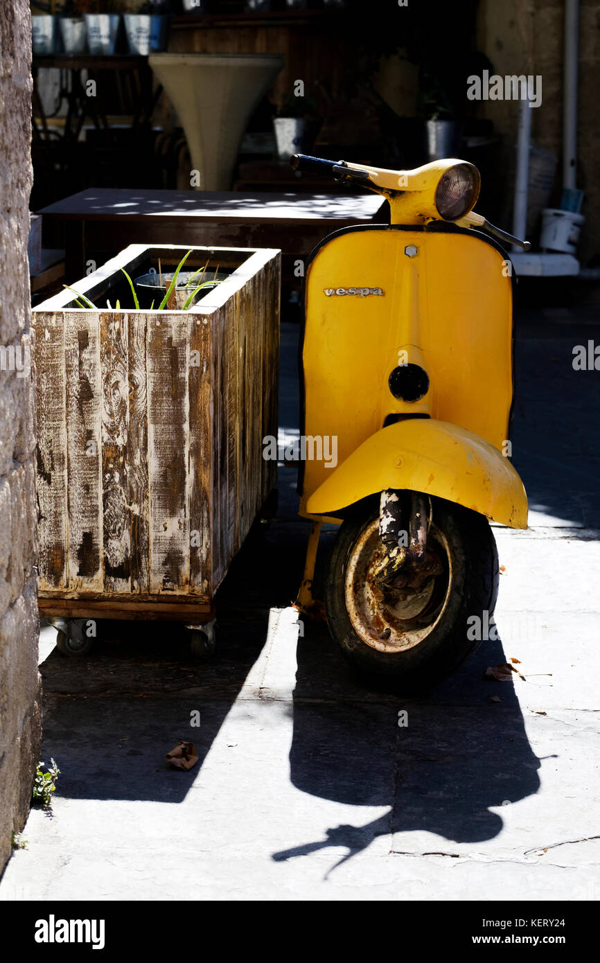 Un vecchio scooter vespa giallo dipinto a mano parcheggiato e incustodito sul marciapiede Foto Stock