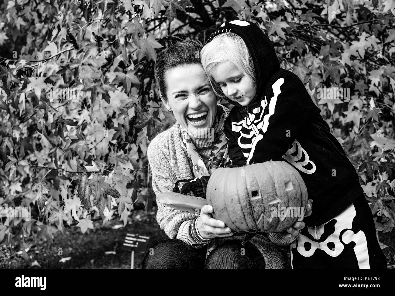 Dolcetto o scherzetto. Felice moderna madre e figlia al parco giocando con scolpita la zucca di Halloween Foto Stock