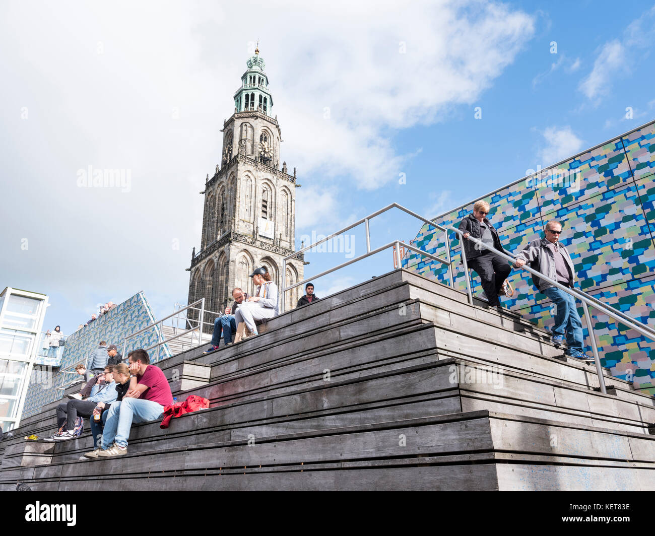 Persone sedersi sui gradini nei pressi della piazza centrale di fronte a torre Martini a Groningen Foto Stock