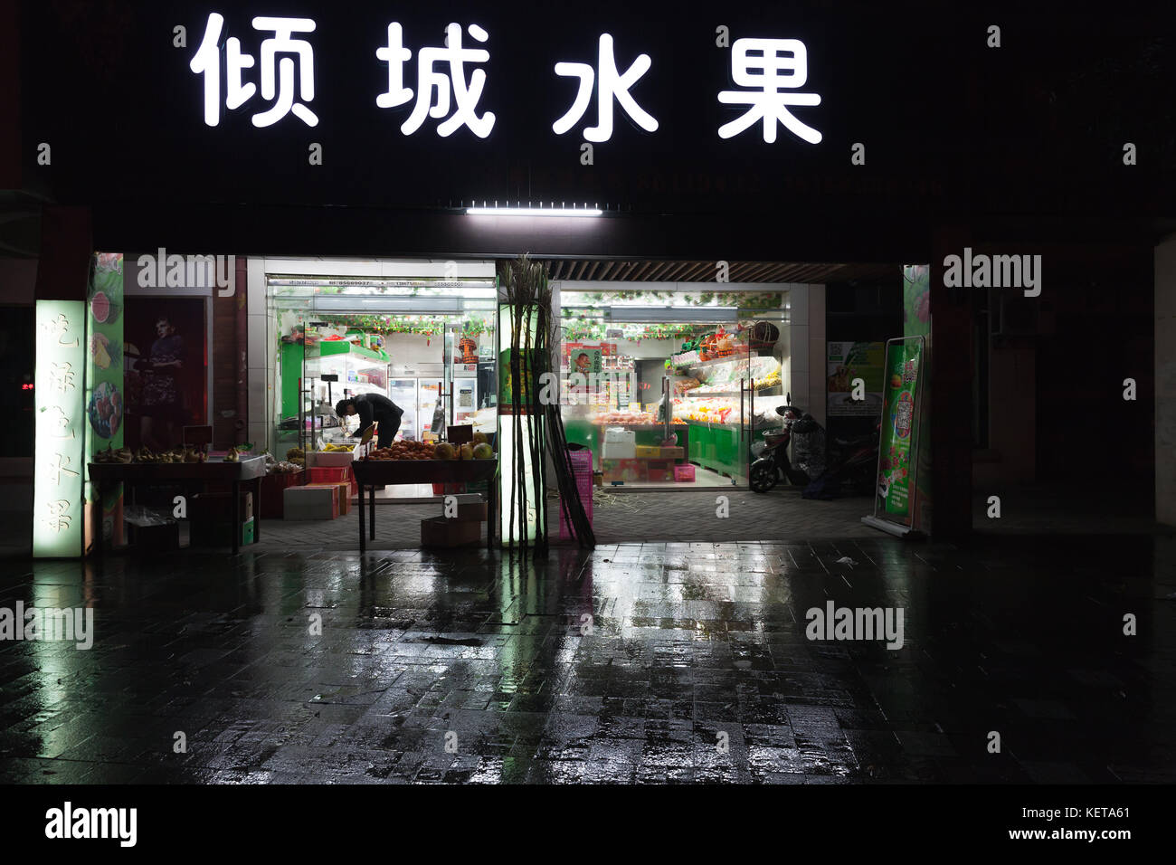 Hangzhou, Cina - 3 dicembre 2014: Piccolo mercato alimentare cinese tradizionale con verdure e pubblicità al neon sul muro. Vista notturna sulla strada Foto Stock