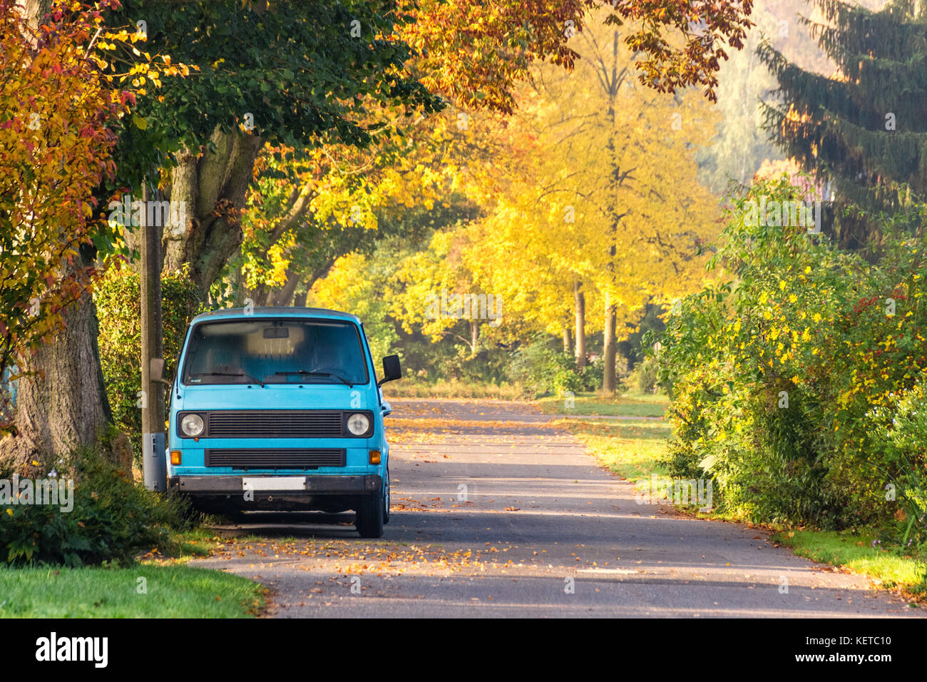 Vintage campeggio auto sulla strada con colori d'autunno fogliame degli alberi. Foto Stock