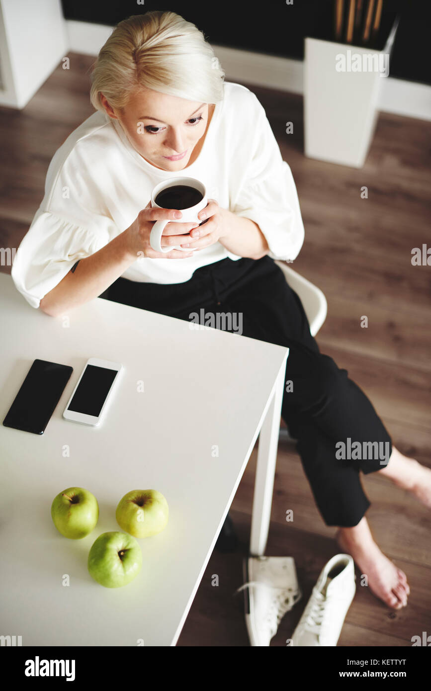 Donna con caffè in appoggio a casa dopo il lavoro Foto Stock