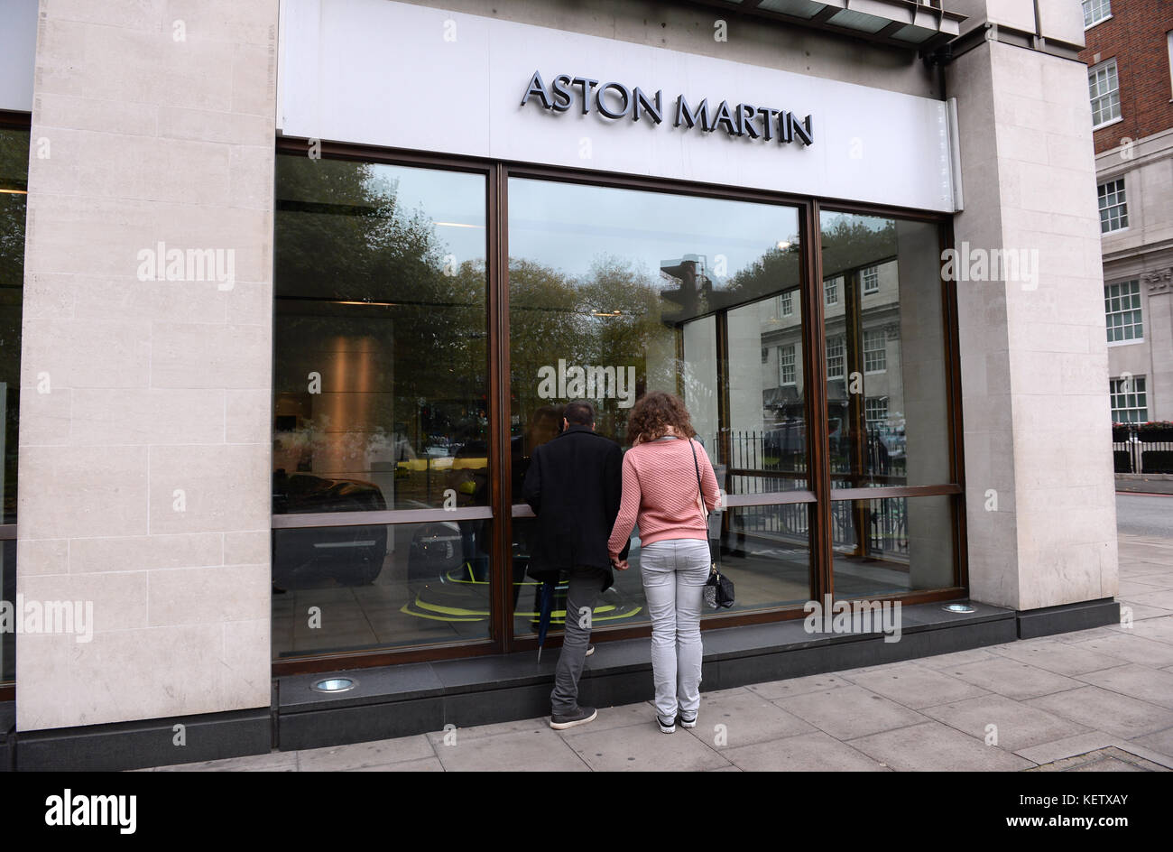 Passers-by guardare nella finestra della concessionaria Aston Martin Mayfair di Stratstone su Park Lane, Londra, la cui società madre, Pendragon, ha visto un tumble nelle sue azioni dopo aver avvertito che i profitti subiranno un colpo dal calo della domanda di nuove automobili in un calo della fiducia dei consumatori. Foto Stock