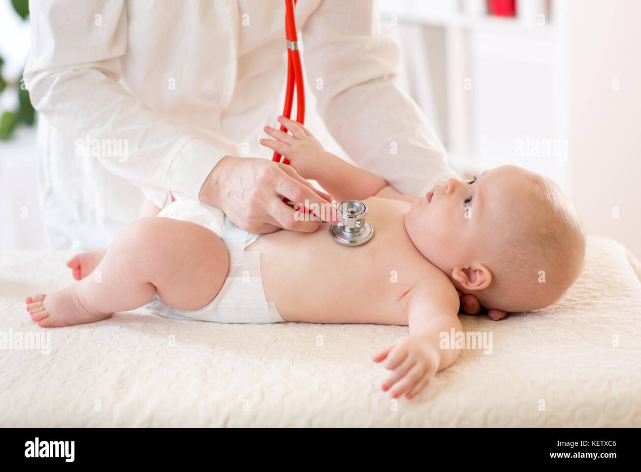 Pediatra esamina baby utilizzando uno stetoscopio per ascoltare il bambino il torace di controllo del battito cardiaco. bambino sta cercando di medico Foto Stock