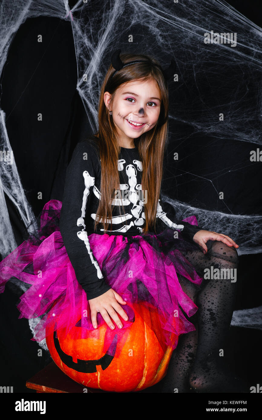 Incantevole piccola ragazza seduta sulla zucca su sfondo nero con una ragnatela Foto Stock