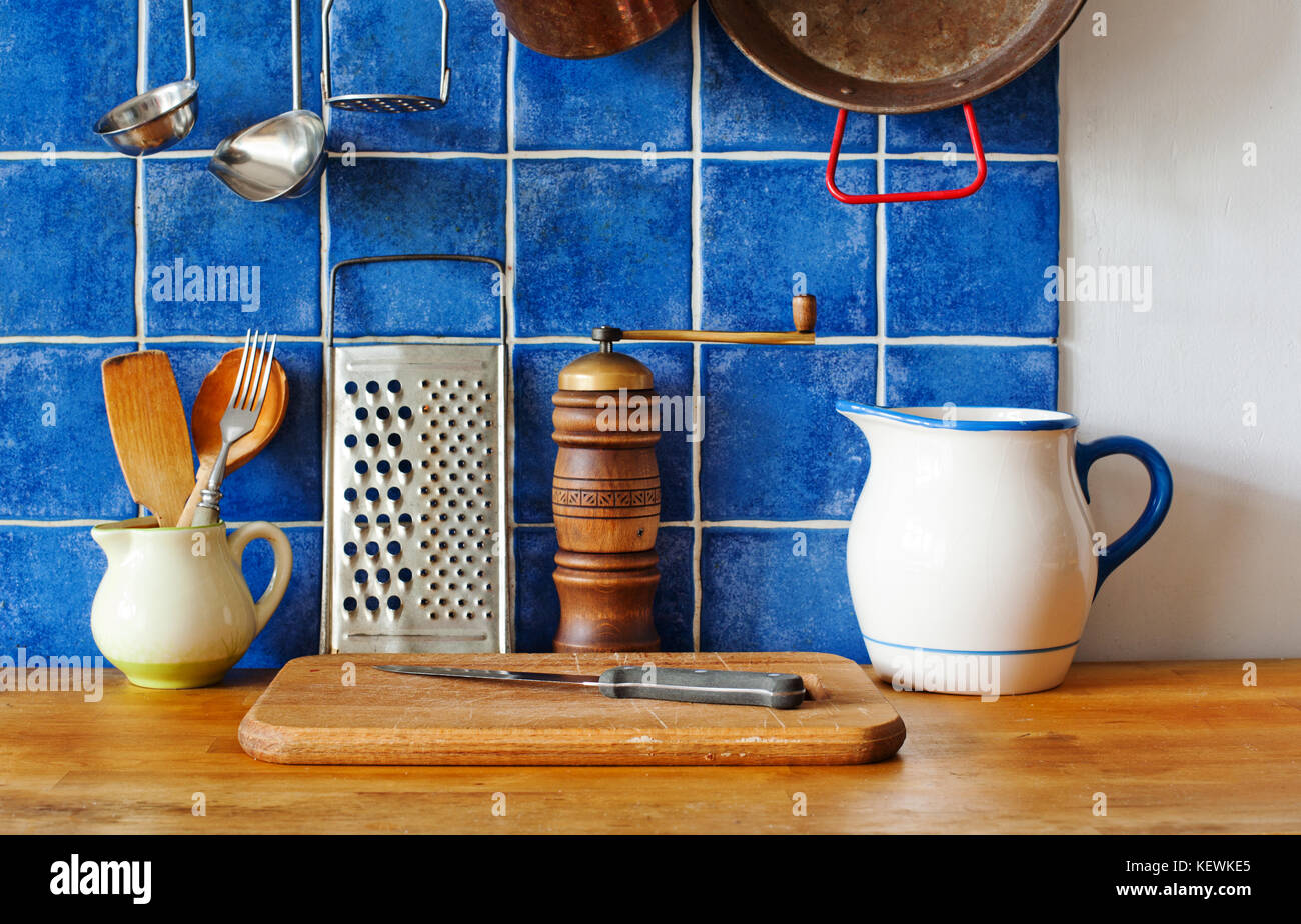 Cucina interno ancora la vita. Vintage ceramica utensili brocche, tagliere,  coltello, un cucchiaio di legno, pepe e metallico grattugia. Blu parete  piastrellata foto di sfondo Foto stock - Alamy