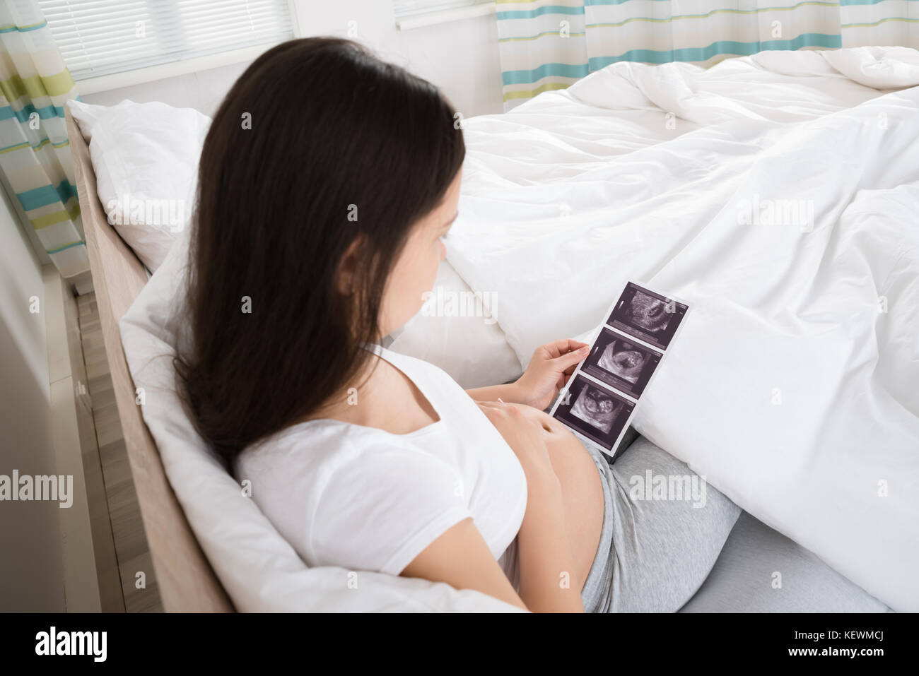 Donna incinta guardando a scansione ad ultrasuoni del bambino nel suo appartamento Foto Stock