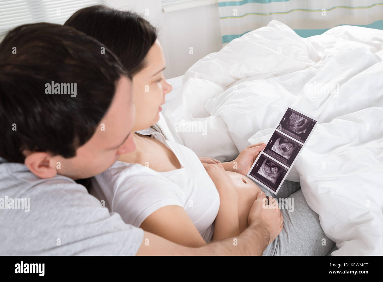 Coppia giovane guardando a scansione ad ultrasuoni di loro aspettano il bambino a casa Foto Stock