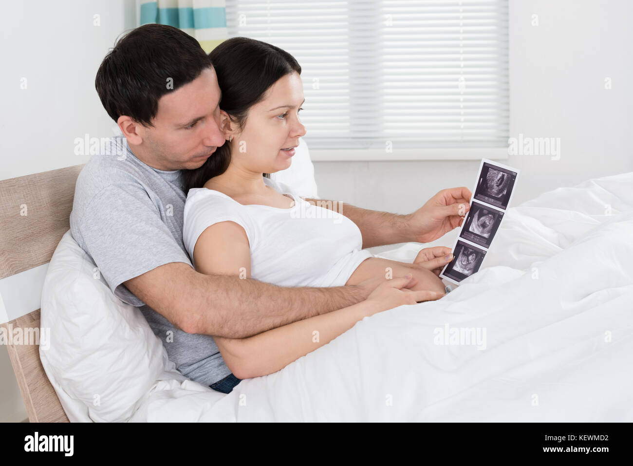Coppia giovane guardando a scansione ad ultrasuoni di loro aspettano il bambino a casa Foto Stock