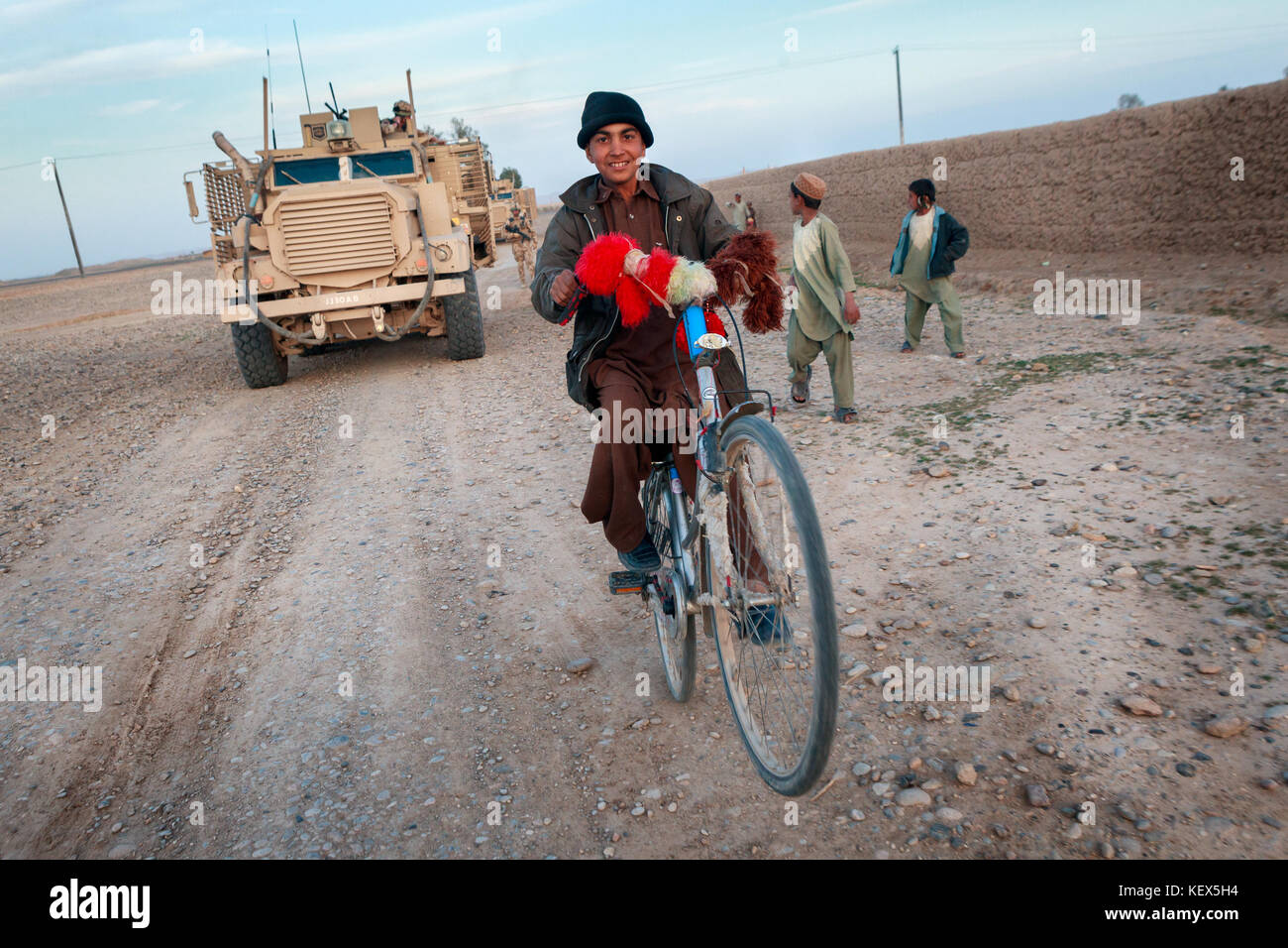 Un giovane ragazzo afghano tira un wheelie come egli corse davanti a un esercito britannico Mastiff veicolo blindato Foto Stock