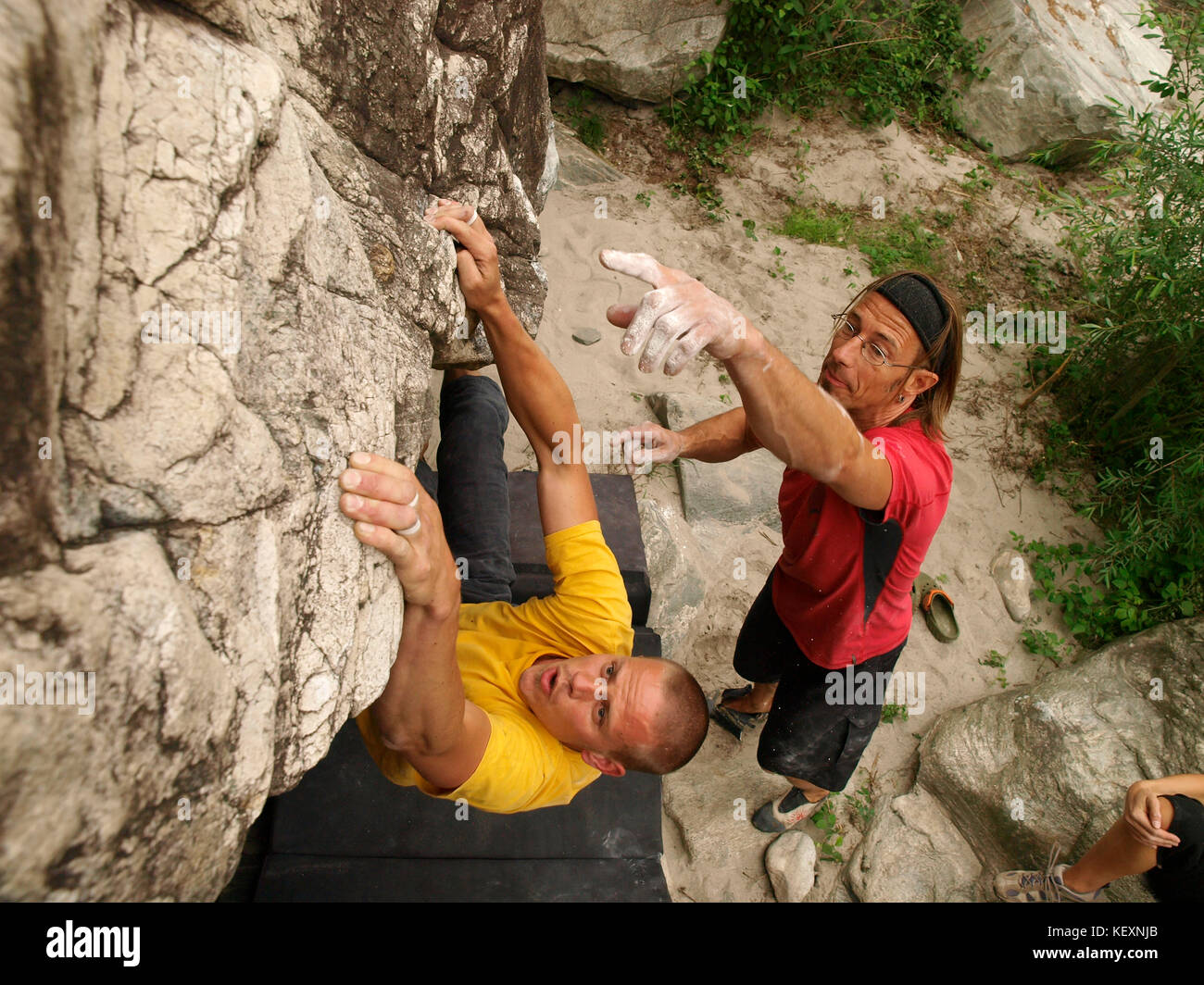 Due uomini sono bouldering in Valle Maggia, una valle di montagna vicino a Locarno nella provincia Svizzero del Ticino. Le rocce in questa regione famosa per il clima caldo, offrono grande arrampicata. Uno scalatore sta tentando di inviare un problema di boulder, l'altra è evidenziata una buona tenuta. Foto Stock