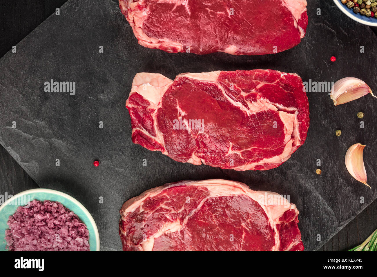 Tre fette di carne cruda su nero con il condimento Foto Stock