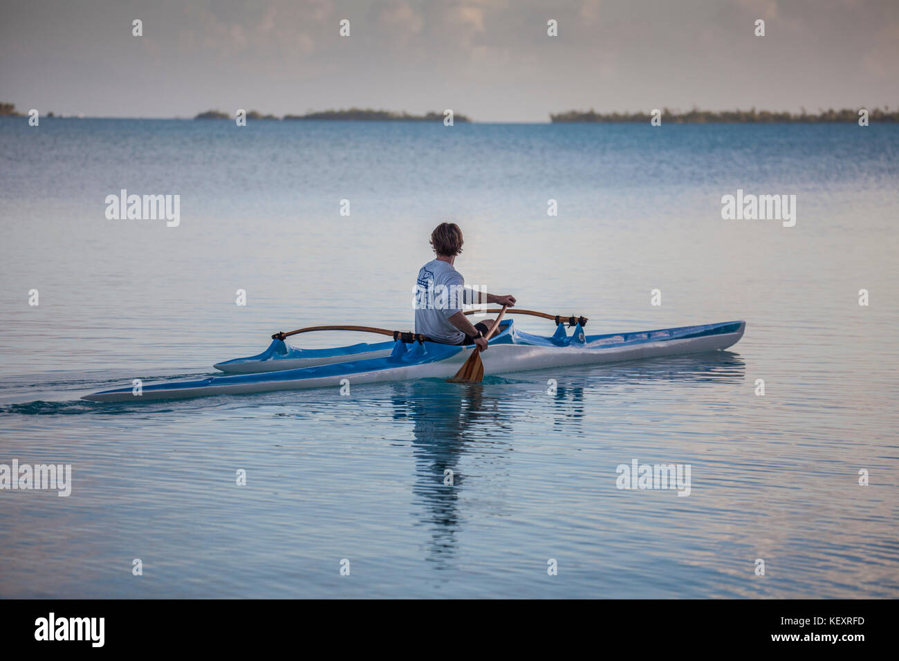 Fotografia del giovane uomo paddling in canoa outrigger al tramonto, Anaa, Polinesia Francese Foto Stock