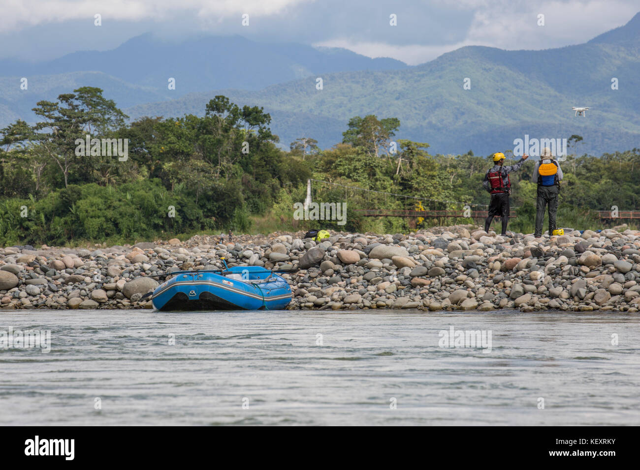 Fotografia con vista posteriore di due uomini guardando drone volare durante un arresto dalla discesa di rafting sul fiume nella giungla nel Parco Nazionale del Manu, Perù Foto Stock
