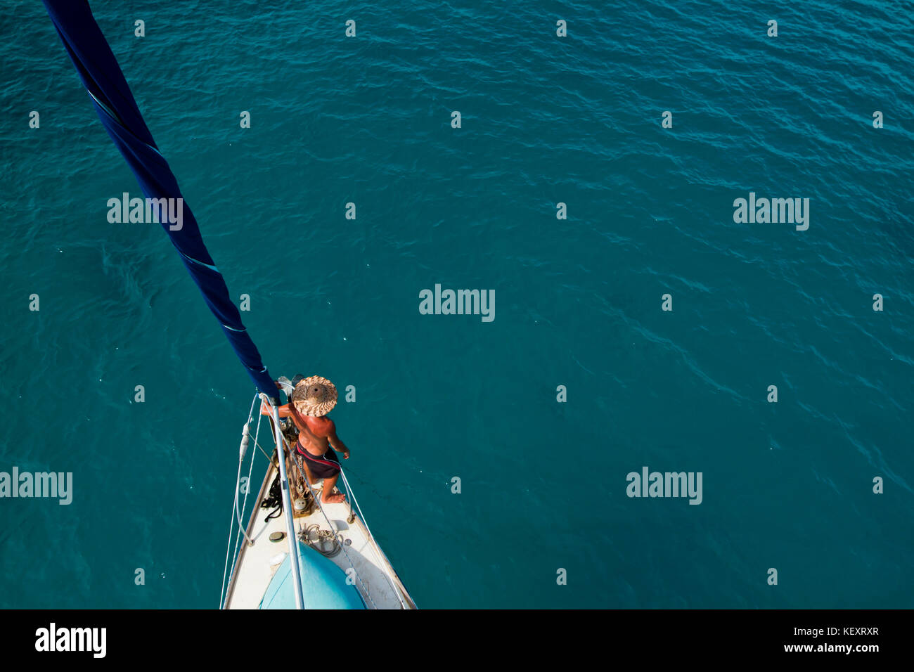Un uomo si appoggia contro il poggiatesta e la vela maestra come visto dall'alto dopo aver avvolto la vela fuori Glovers Reef sulla costa del Belize. Foto Stock
