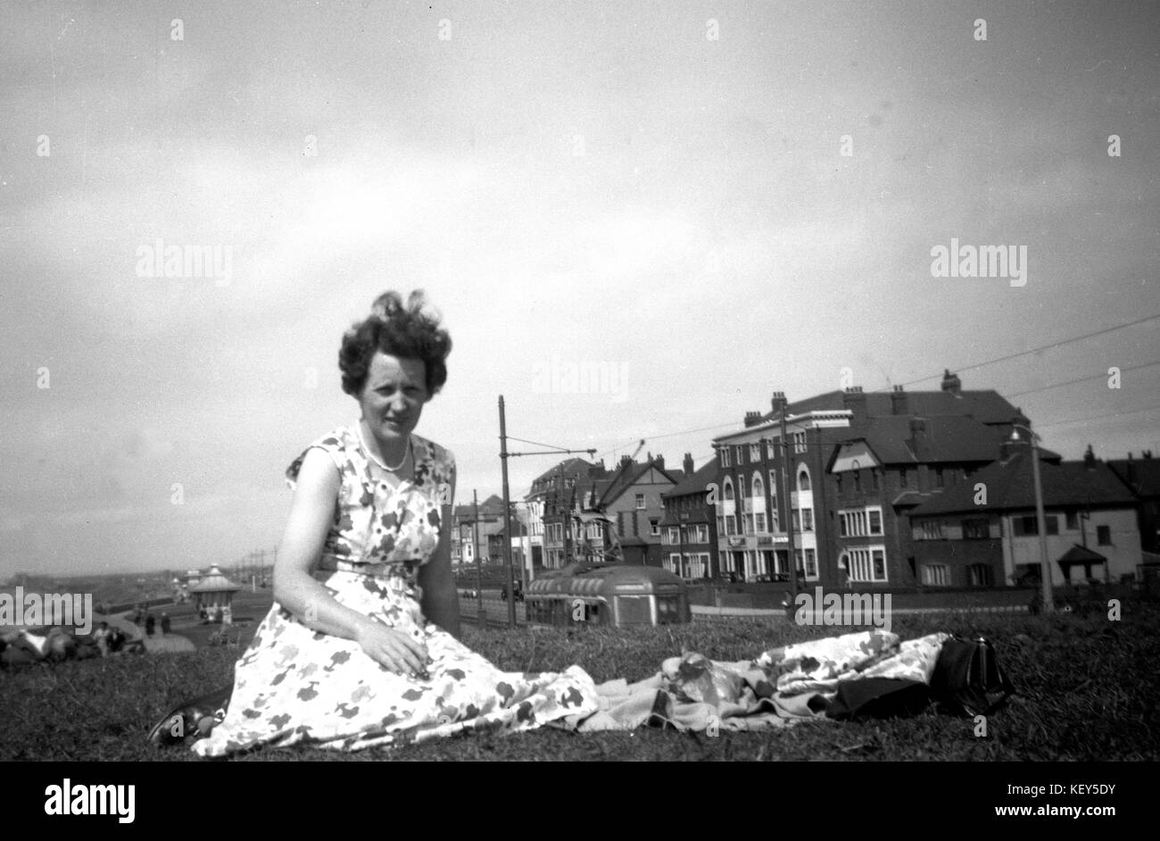 Una donna si rilassa su una banca erbosa in un abito splendiod sul lungomare nel Regno Unito c1949. fotografia di tony henshaw Foto Stock