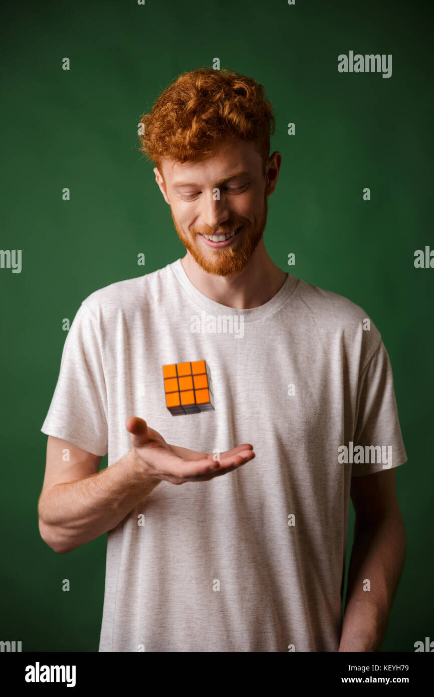 Colpo di giovani readhead sorridente uomo barbuto, tenendo il cubo di Rubik, su sfondo verde Foto Stock