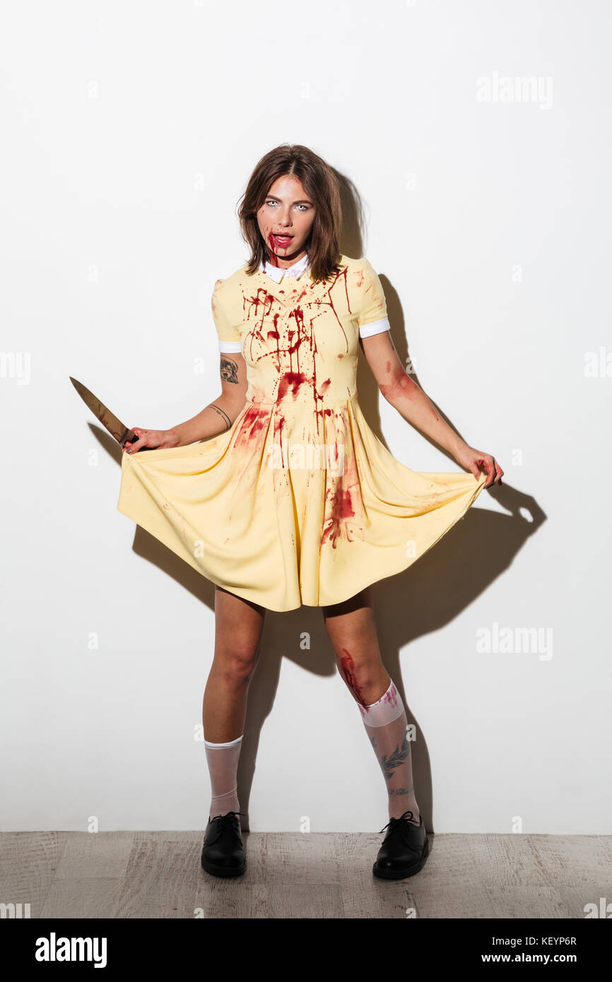 Lunghezza completa immagine di spaventoso zombie donna nel vestire con coltello guardando la telecamera su sfondo bianco Foto Stock