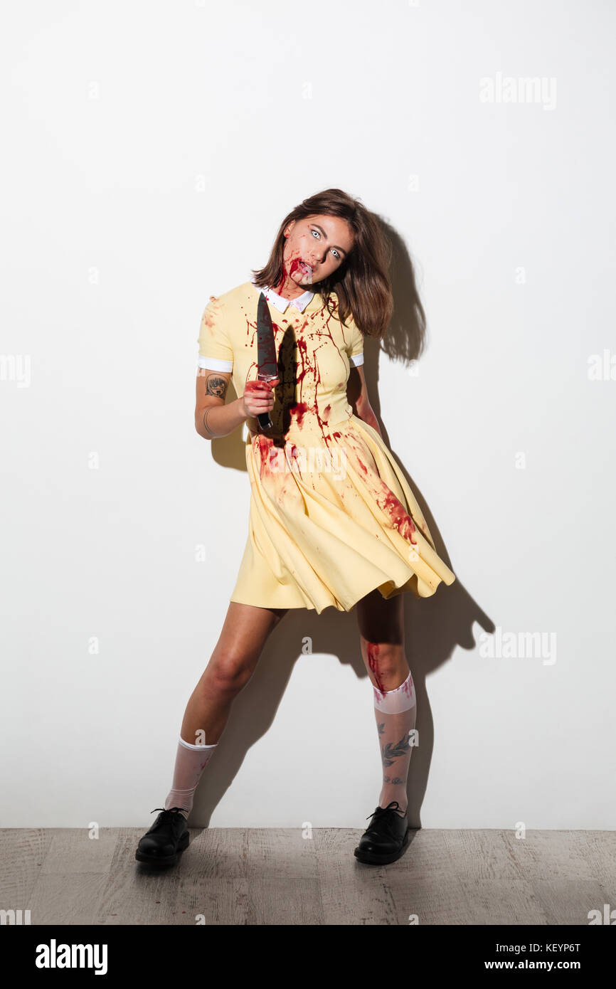 Lunghezza completa immagine di crazy zombie donna nel vestire con coltello guardando la telecamera su sfondo bianco Foto Stock