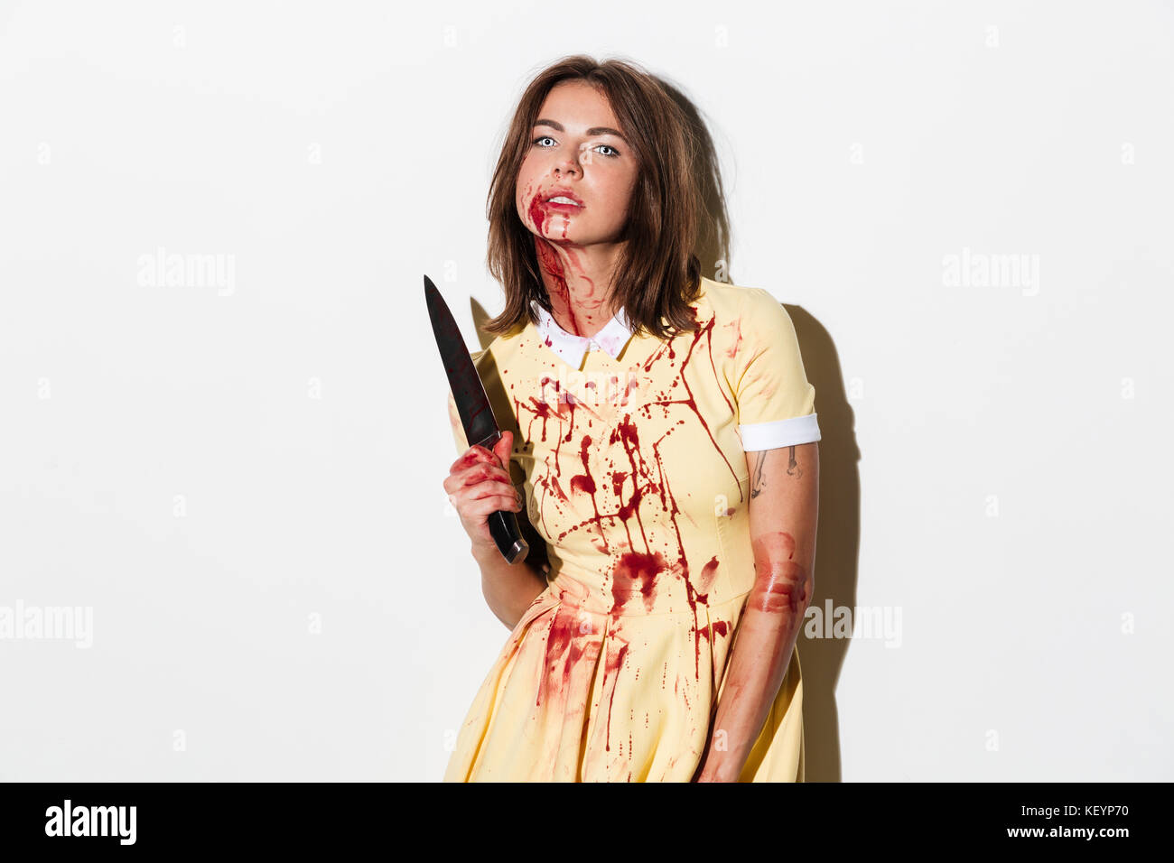 Crazy zombie donna nel vestire tenendo il coltello e guardando la telecamera su sfondo bianco Foto Stock