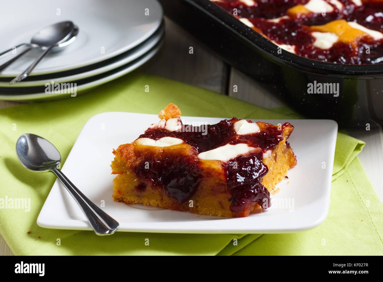 Pezzo di torta con formaggio caserario e marmellata di frutta su piccolo piatto bianco. Più piatti e vassoio da forno nero con la torta sullo sfondo Foto Stock