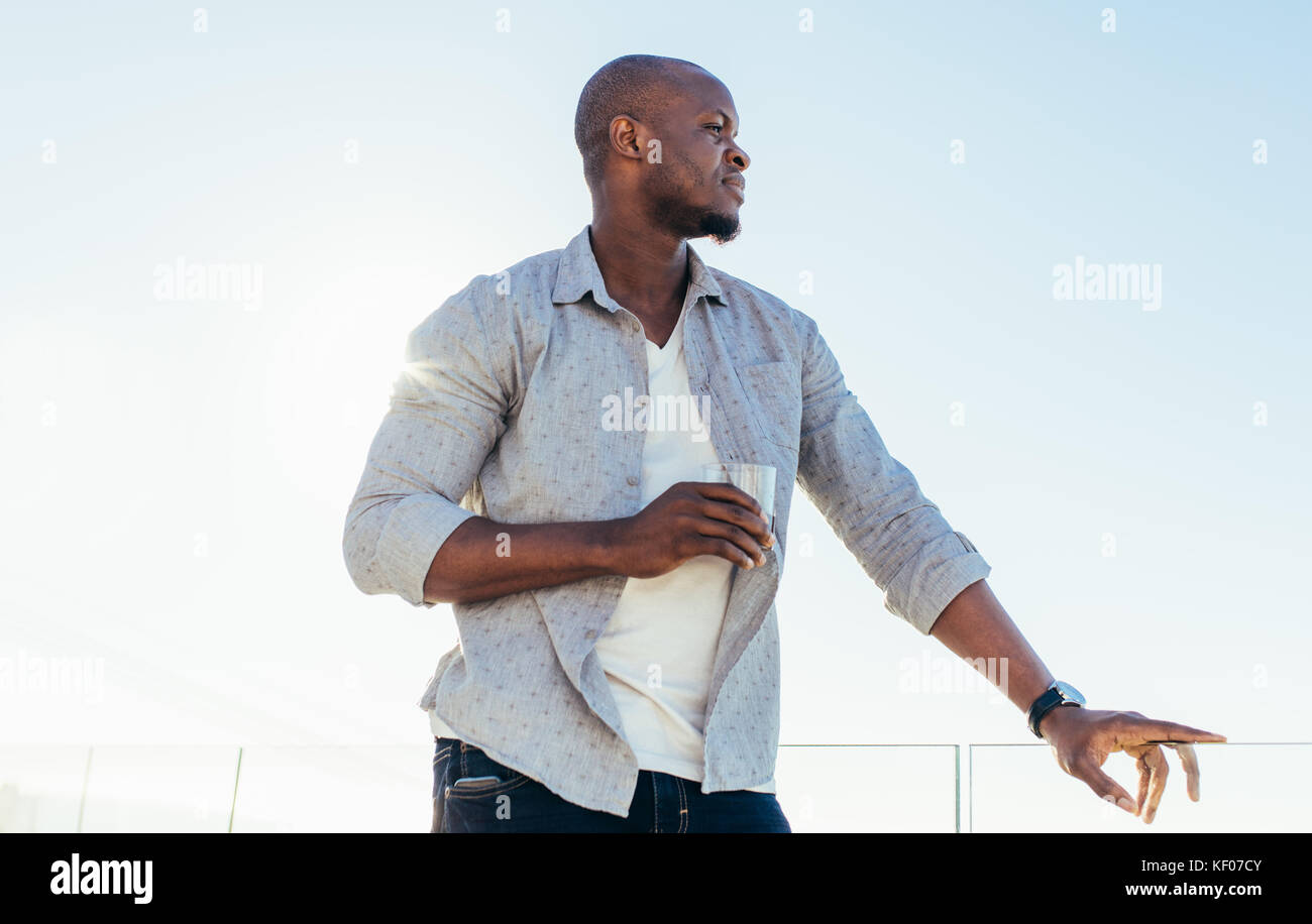 Uomo su una vacanza gustando un bicchiere di vino. Uomo in piedi con un bicchiere di vino con cielo blu chiaro in background. Foto Stock