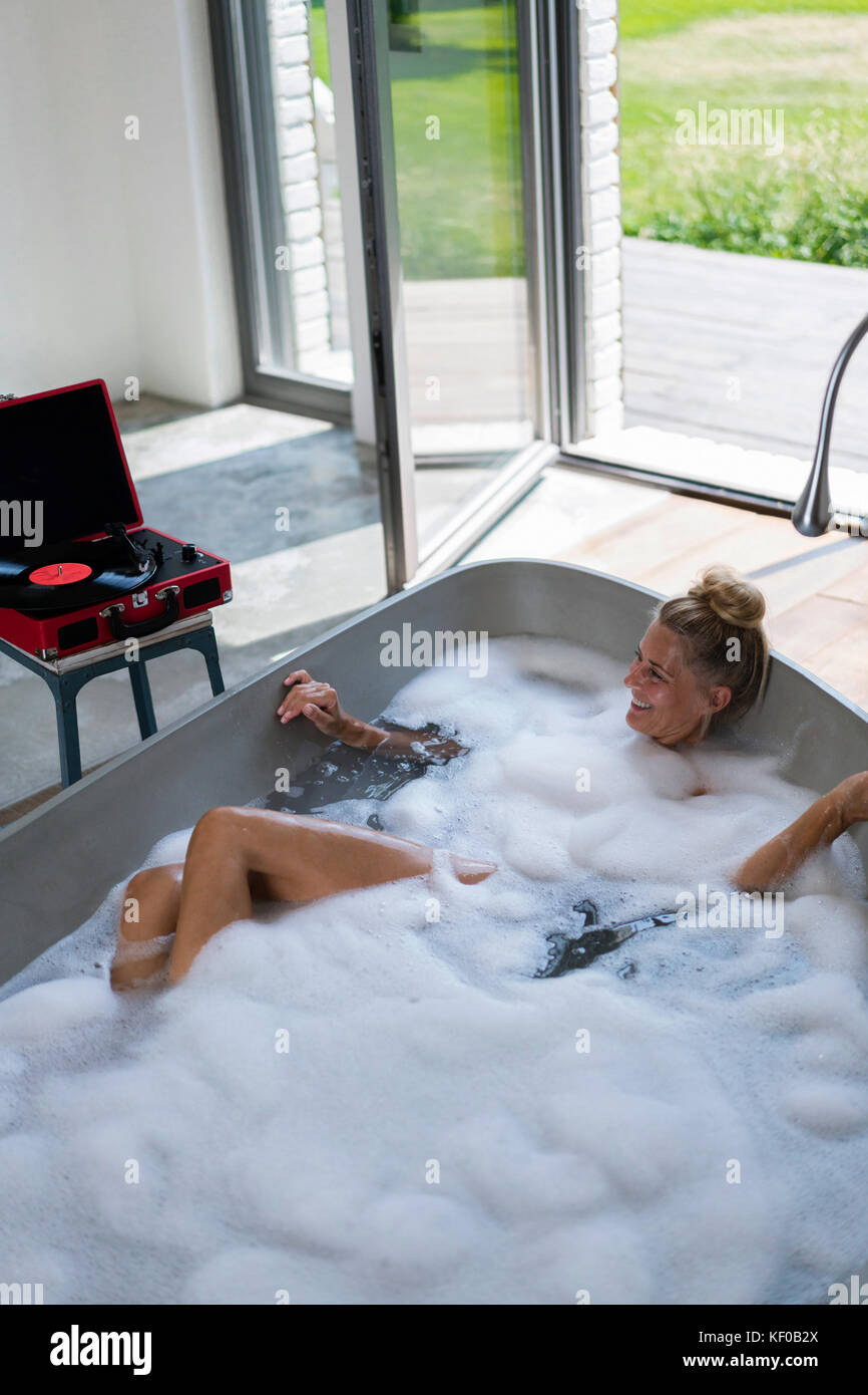 Donna matura tenendo bubble bath, ascoltando musica da analogico record giocatore Foto Stock