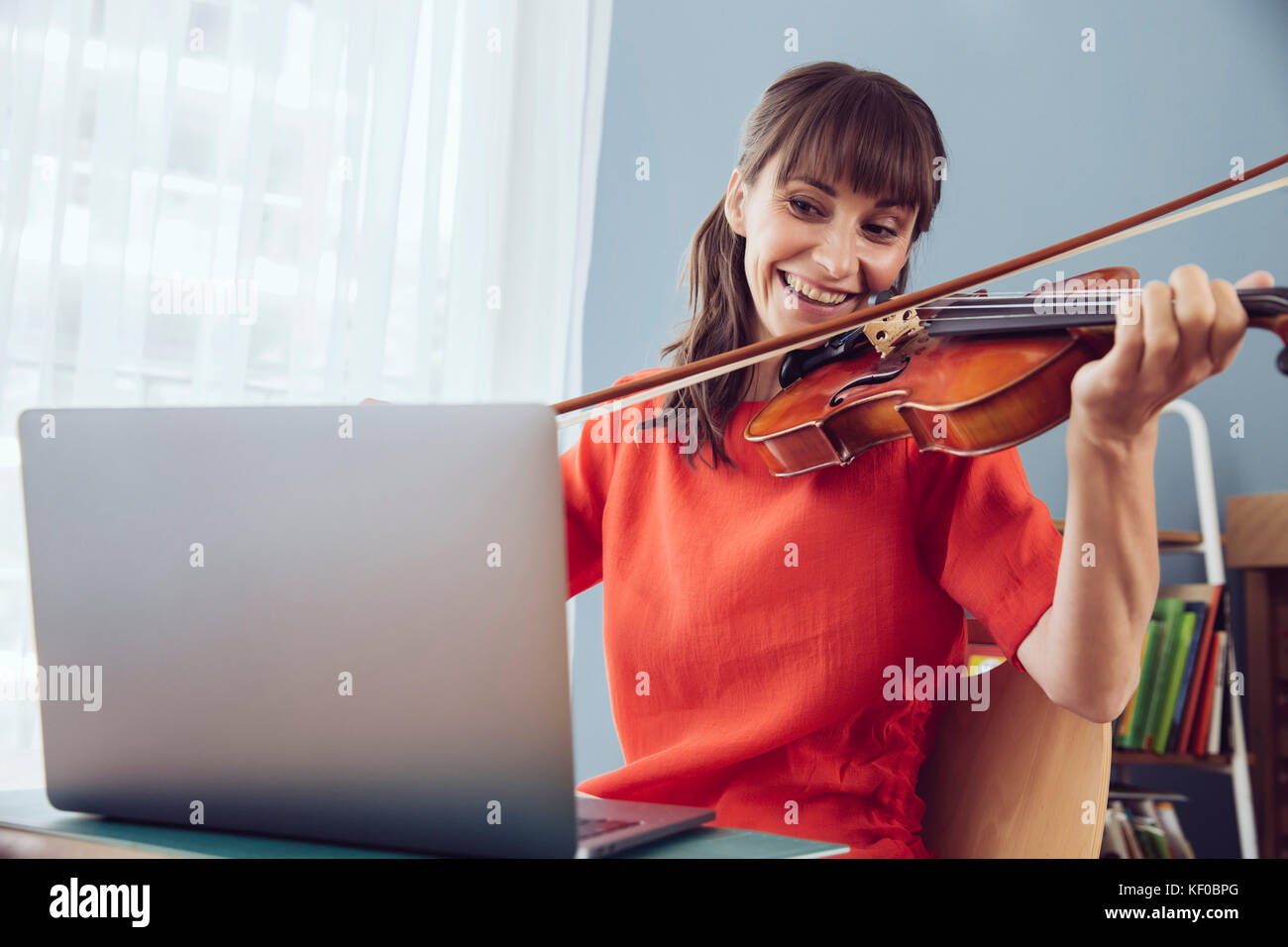 Donna che utilizza computer portatile per la riproduzione di un brano su un violino Foto Stock