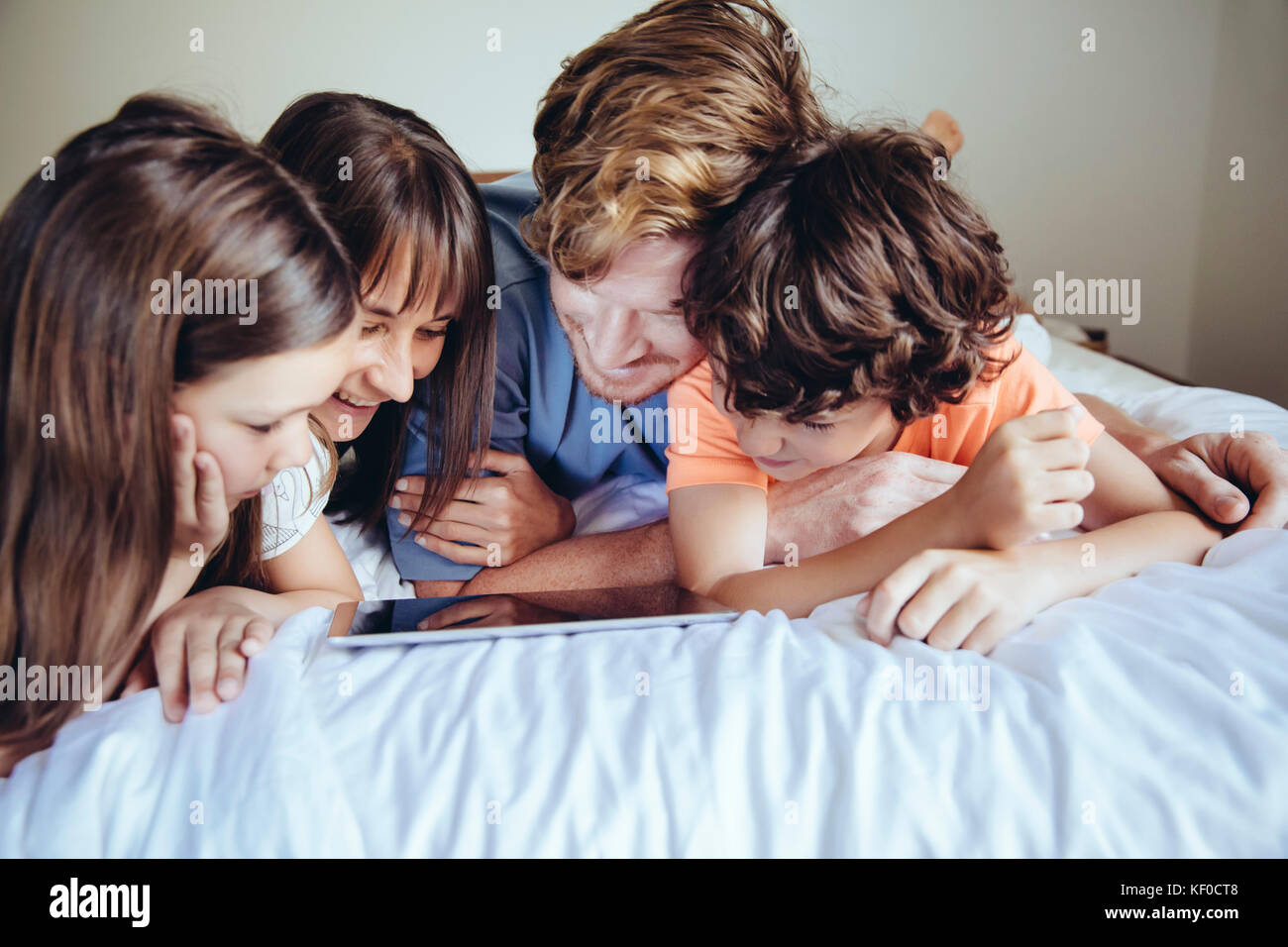 I bambini e i loro genitori guardando il tablet sul letto Foto Stock