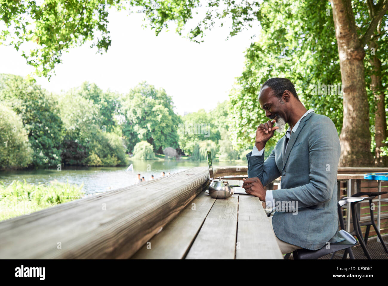 Londra, UK, oltre 50s africano nero maschio divertirsi lavorando sul suo laptop all'aperto, singolo. Foto Stock