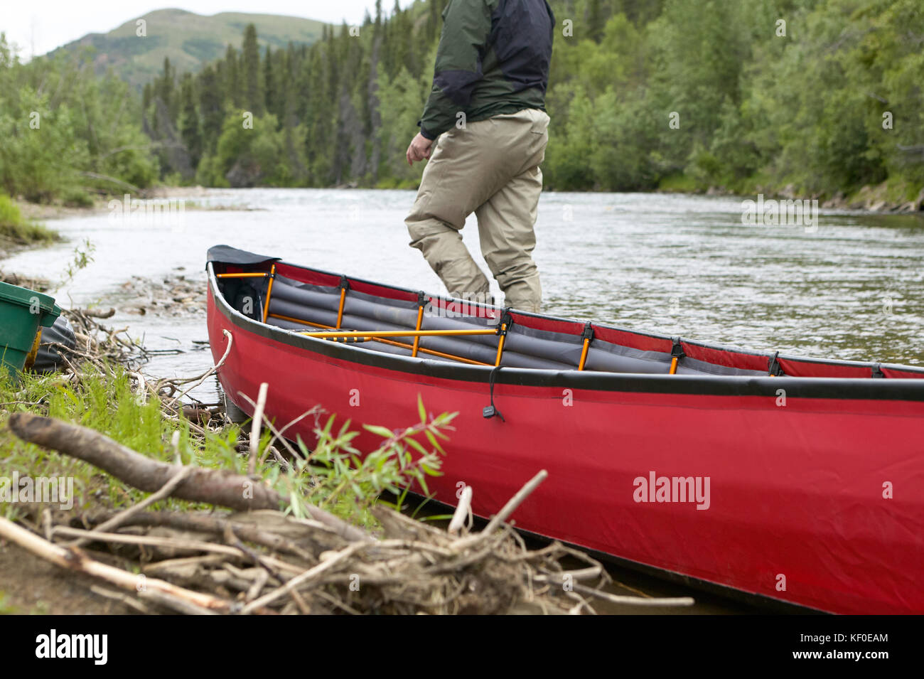 Una chiusura del raccolto di una persona e un spiaggiata, rosso canoa gonfiabile su una remota alaskan river. Foto Stock