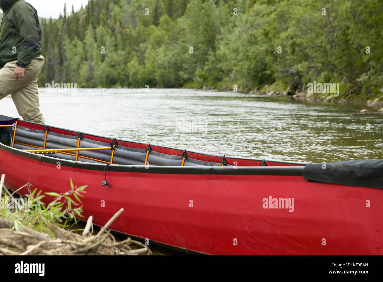 Una chiusura del raccolto di una persona e un spiaggiata, rosso canoa gonfiabile su una remota alaskan river. Foto Stock