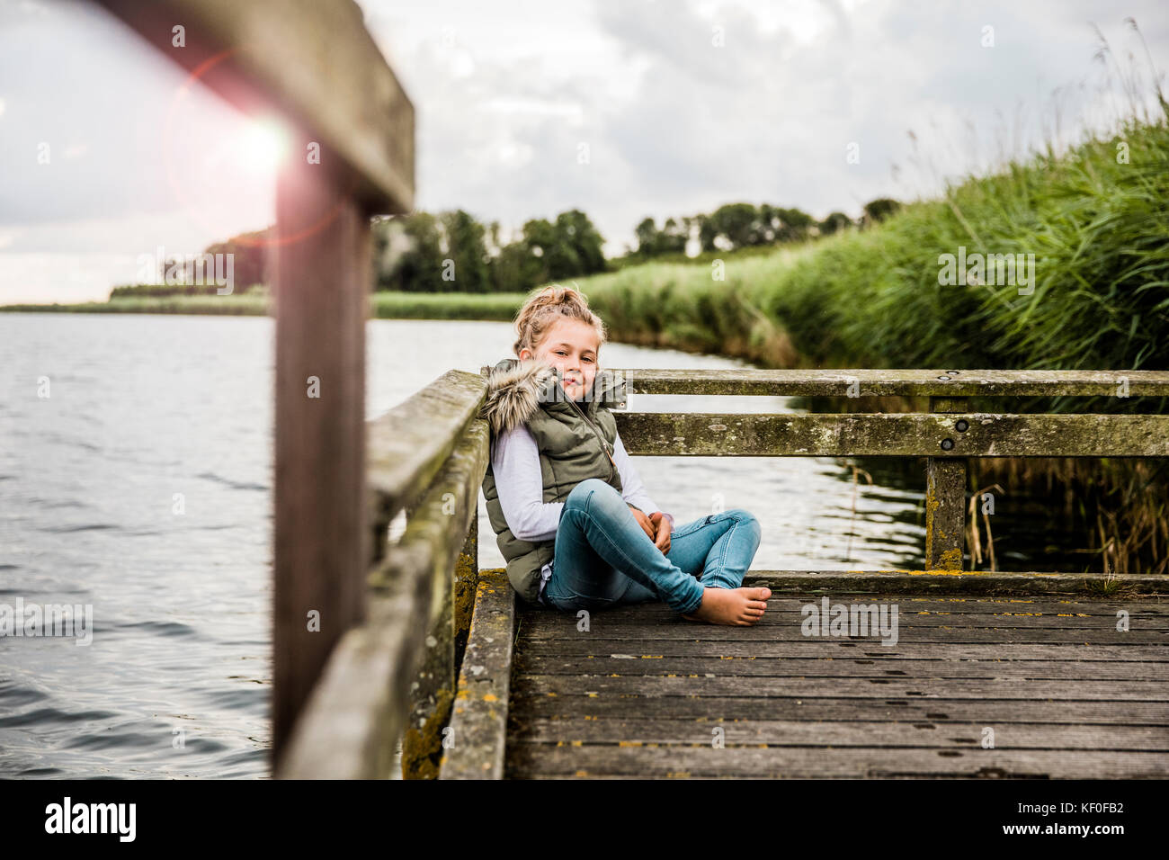 Ragazza seduta sul molo al lago Foto Stock