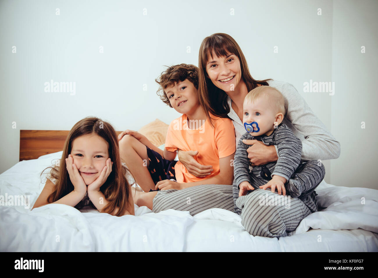 Felice madre nel letto con i suoi tre bambini Foto Stock