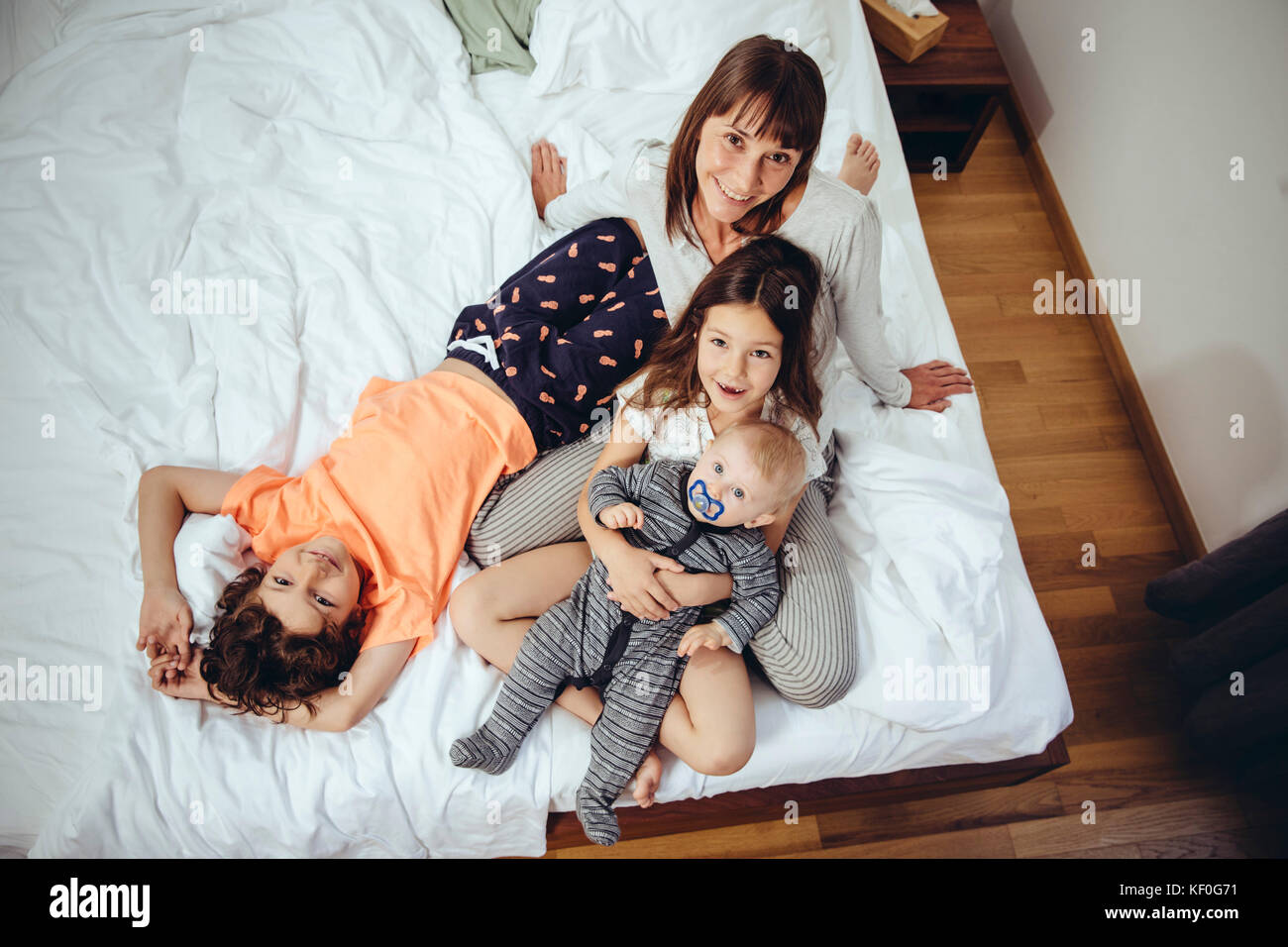 Felice madre nel letto con i suoi tre bambini Foto Stock