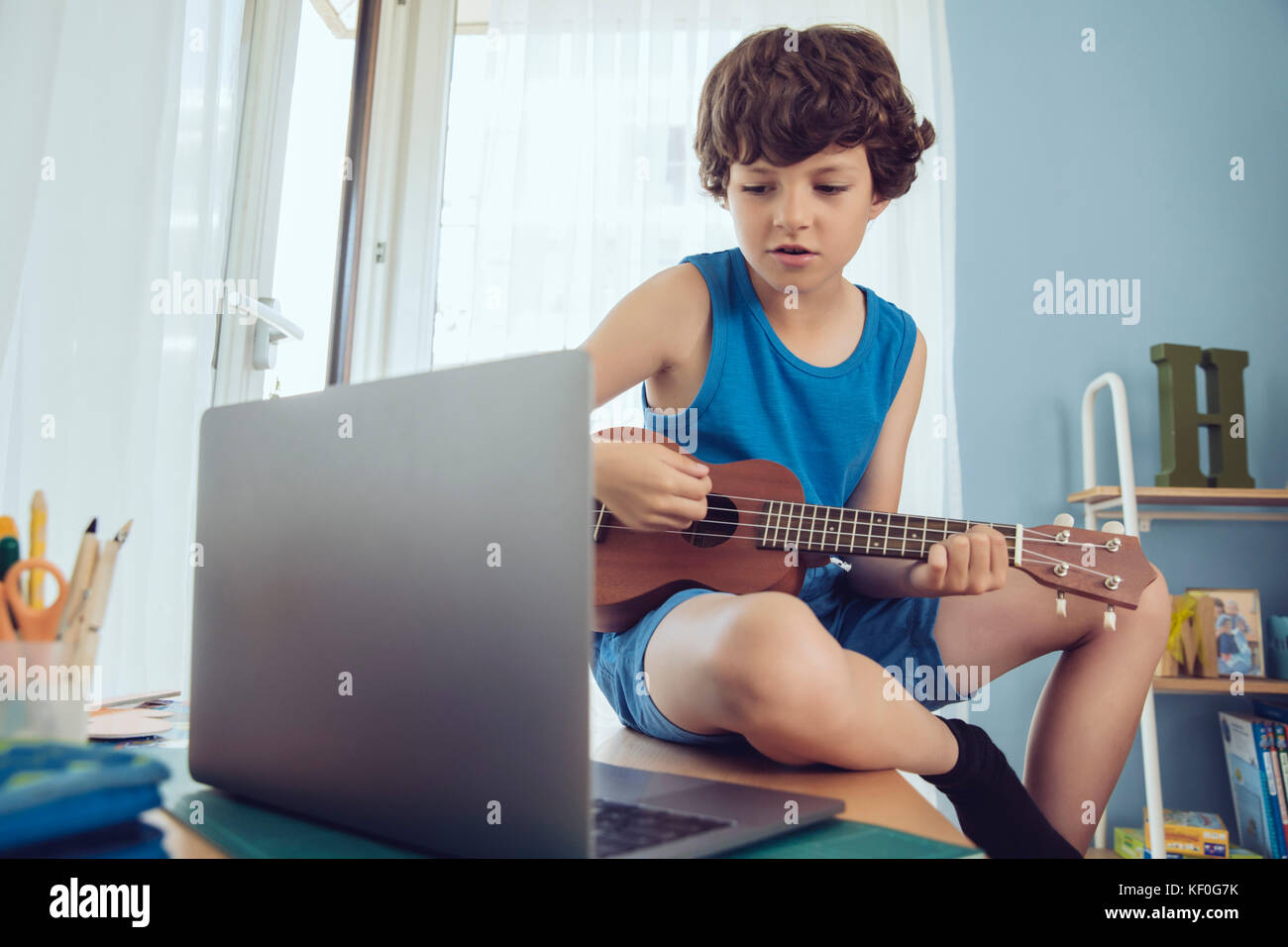 Boy utilizzando computer portatile per la riproduzione di un brano su un ukulele Foto Stock