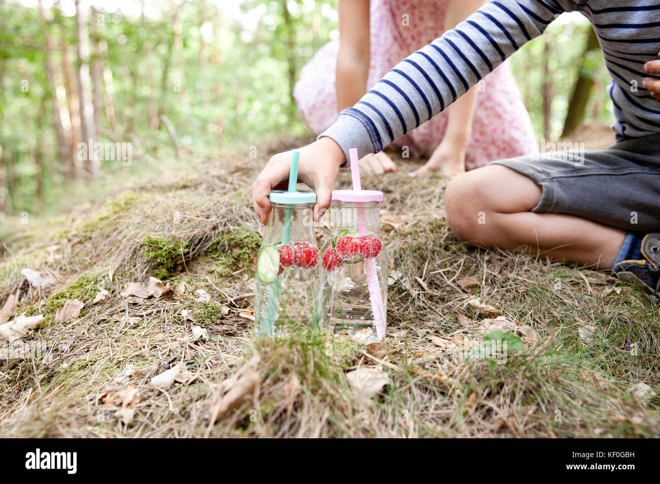 Ragazzo di raggiungere per il vetro di acqua infusa con fette di cetriolo e lamponi in foresta Foto Stock