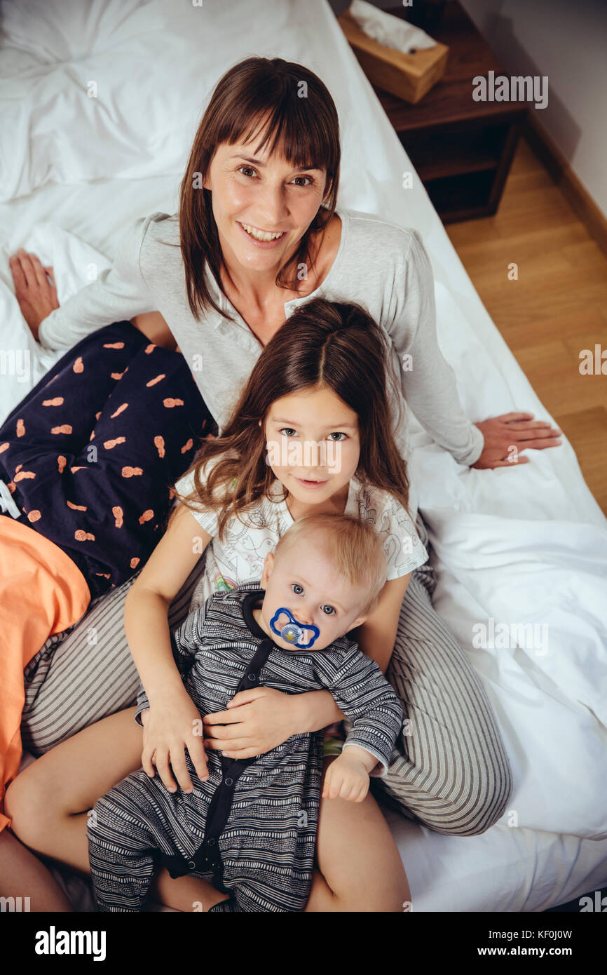Felice madre nel letto con i suoi tre bambini Foto Stock