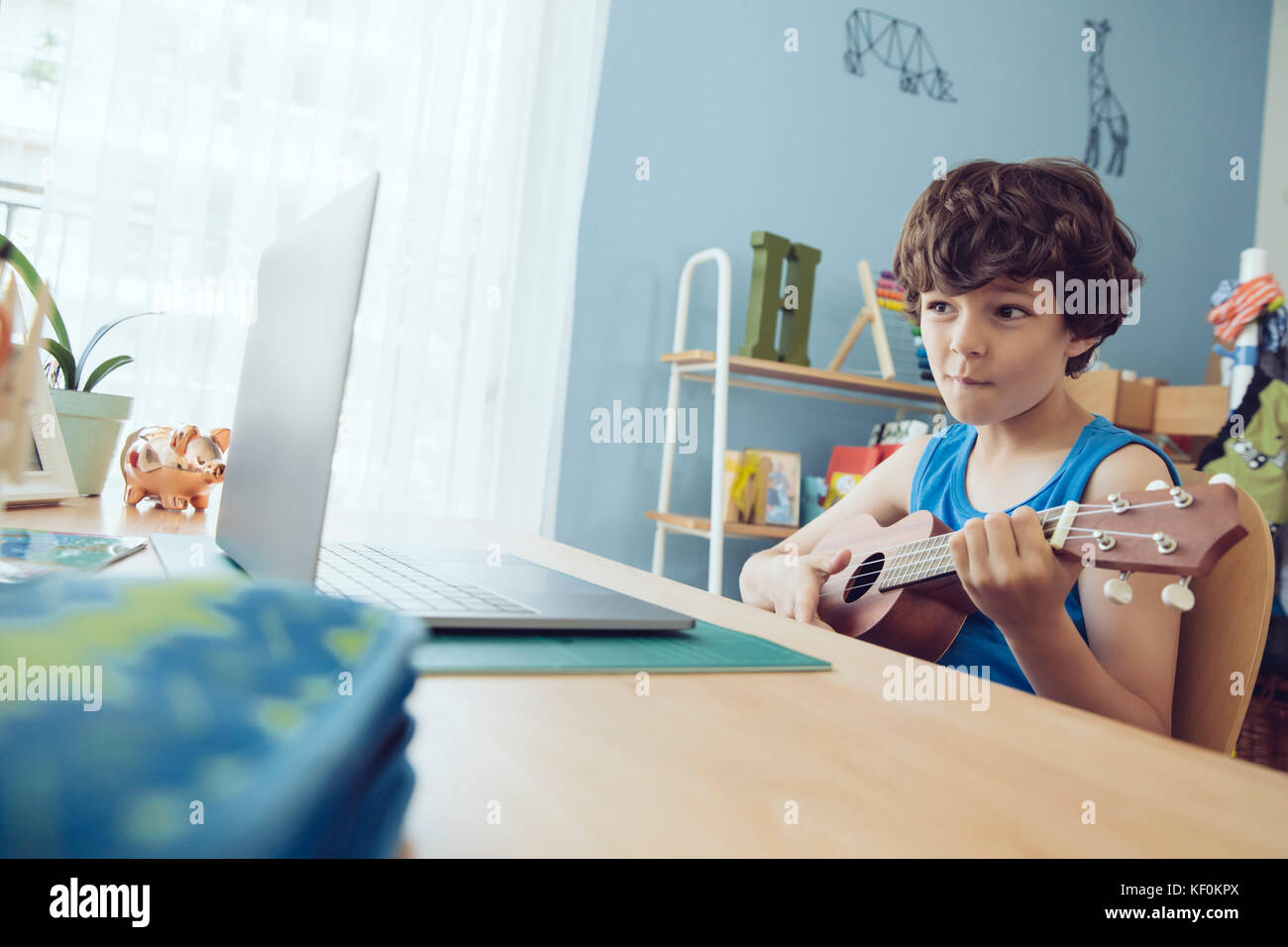 Boy utilizzando computer portatile per la riproduzione di un brano su un ukulele Foto Stock
