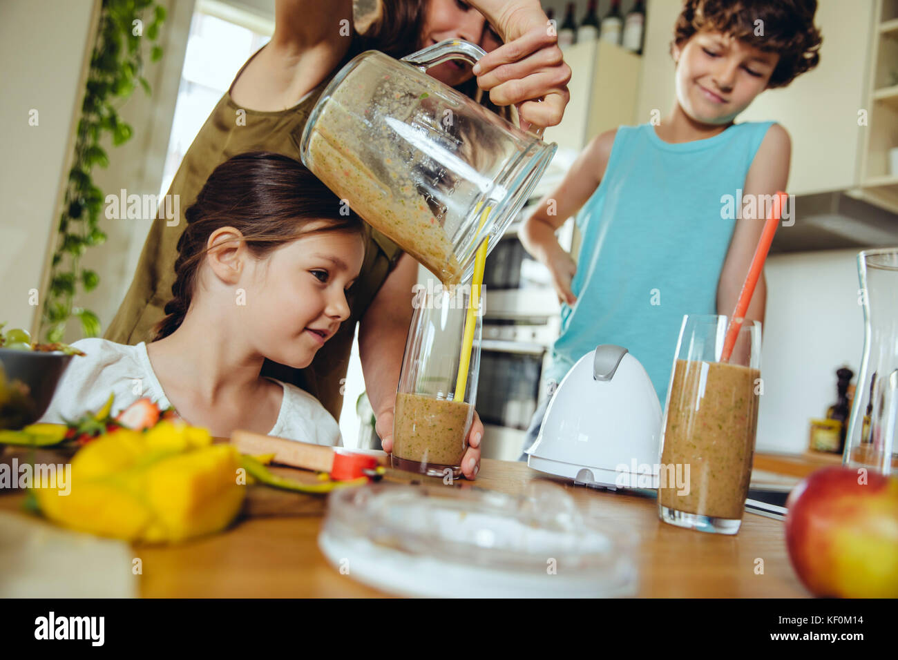 Madre di due bambini versando un smoothie in bicchieri Foto Stock