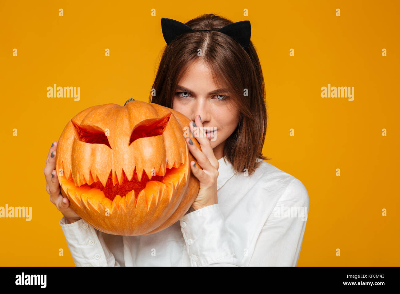 Immagine di grave giovane donna vestita di crazy cat costume di halloween su sfondo giallo con la zucca. Foto Stock