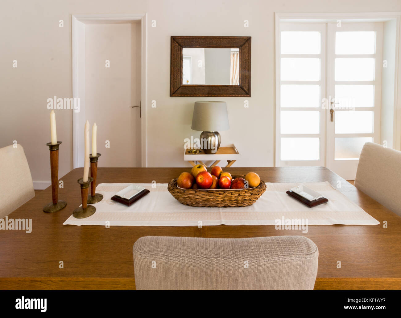 Un tavolo da pranzo in legno con candele, un cesto di bambù con frutta e quattro sedie. Foto Stock