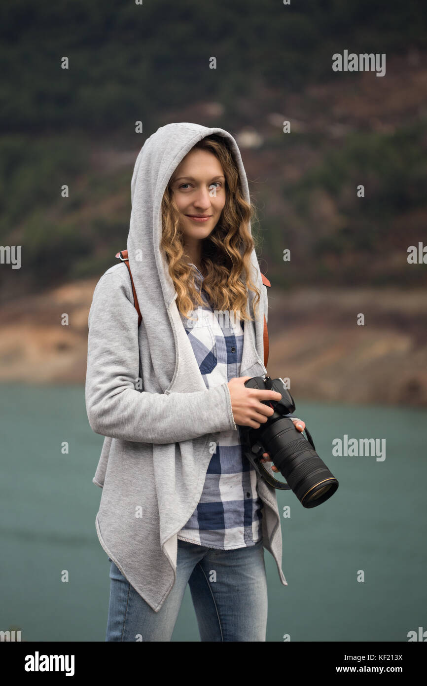 Donna bionda fotografo indossano jeans, controllato maglietta e felpa con  cappuccio grigio azienda focale lunga Foto stock - Alamy