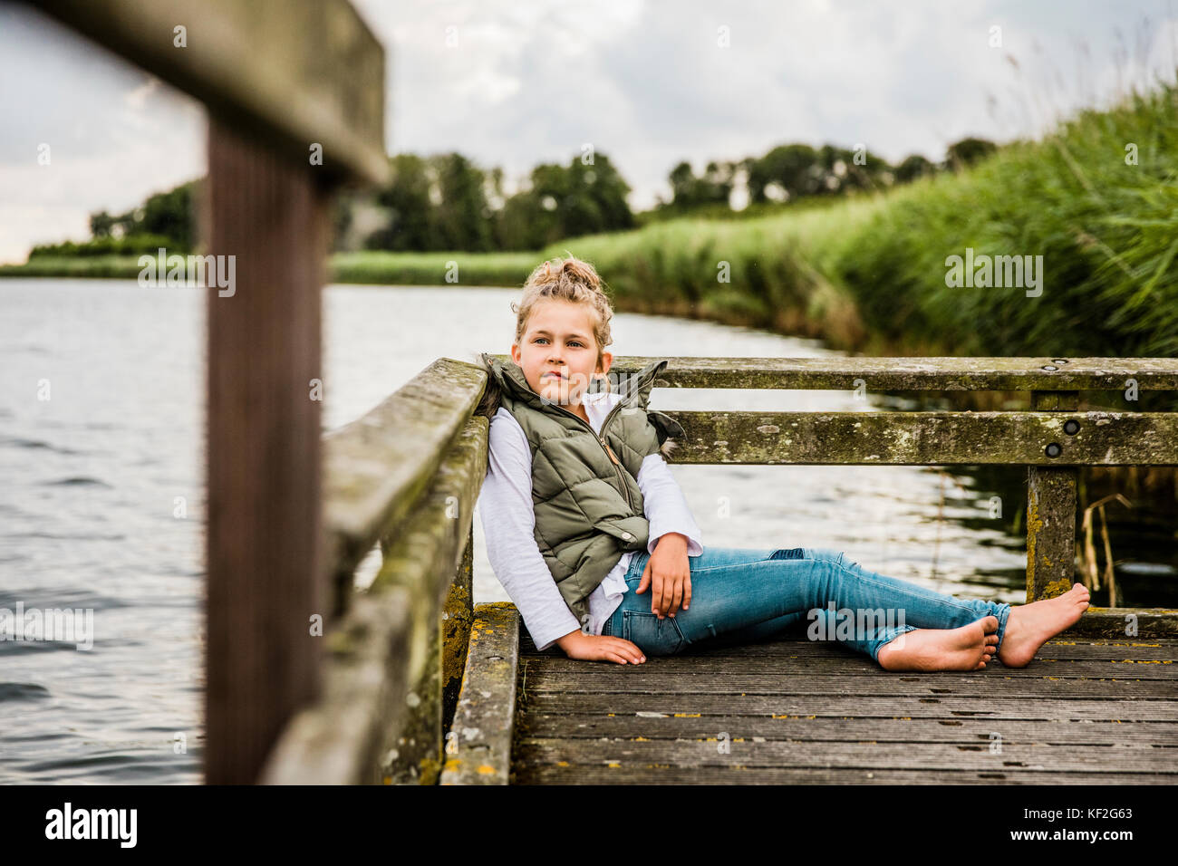 Ragazza seduta sul molo al lago Foto Stock