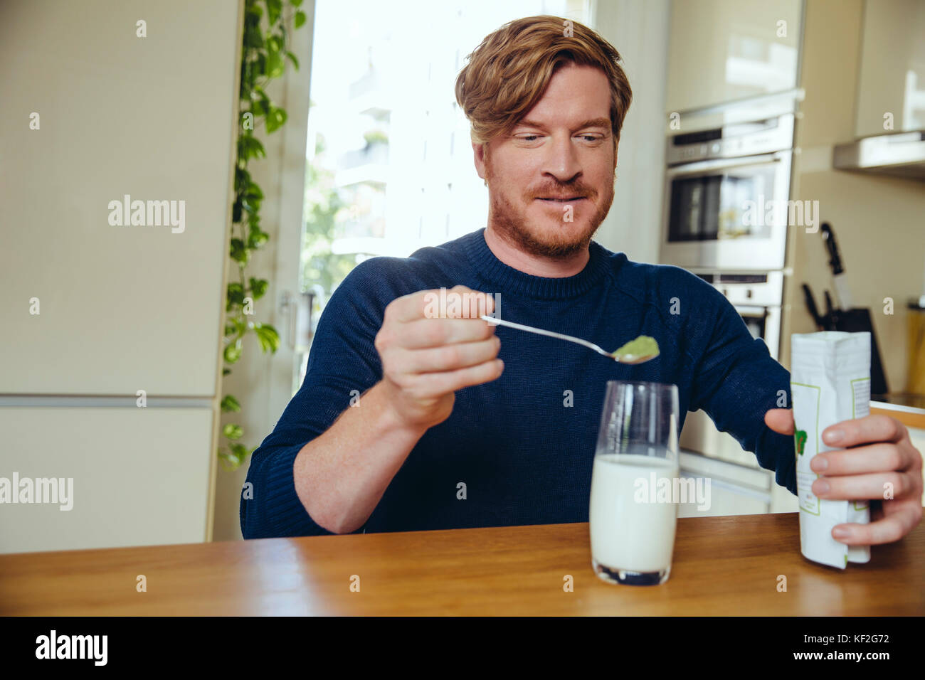 L'uomo mettendo sana sostanza verde in un bicchiere di latte Foto Stock