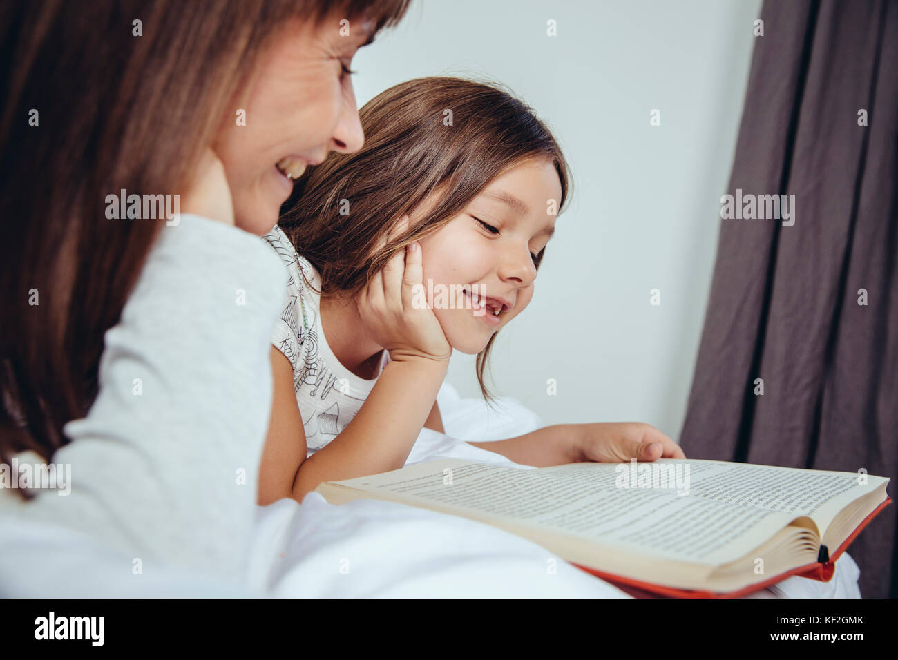 Madre e figlia libro di lettura a letto Foto Stock