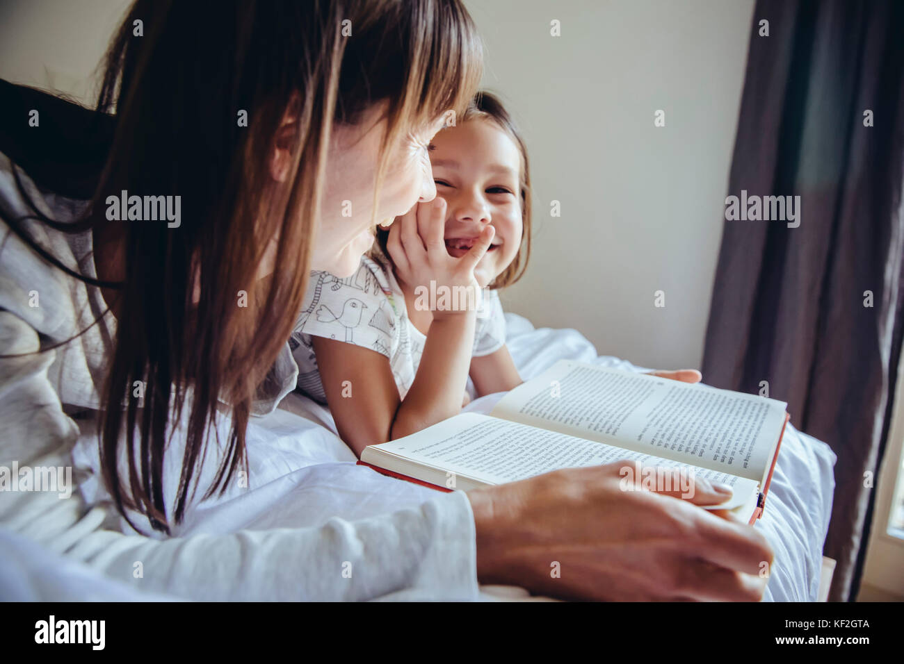 Madre e figlia libro di lettura a letto Foto Stock